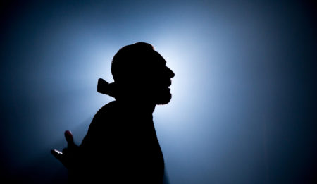 Silhouette of a man in profile. He is wearing what looks like a cloak with a large collar.