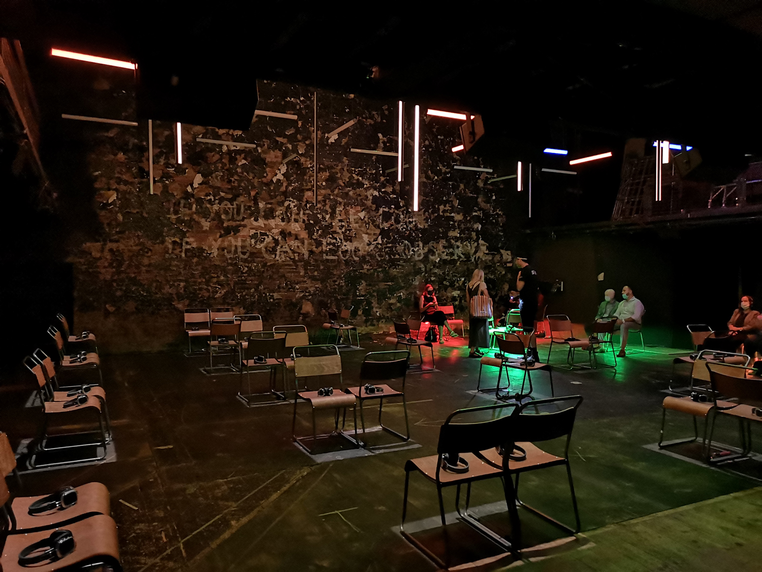 A black box theatre space with pairs of seats placed apart across the stage