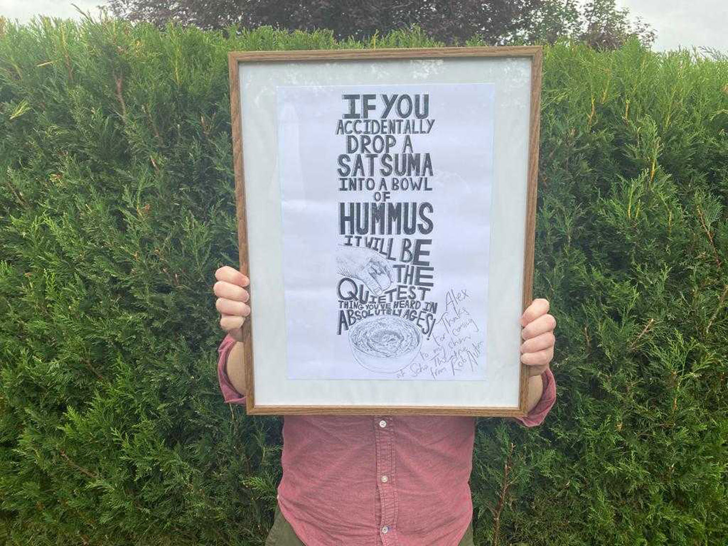 Alex from Cog holds up an illustrated print in a wooden frame signed by the artist Rob Auton