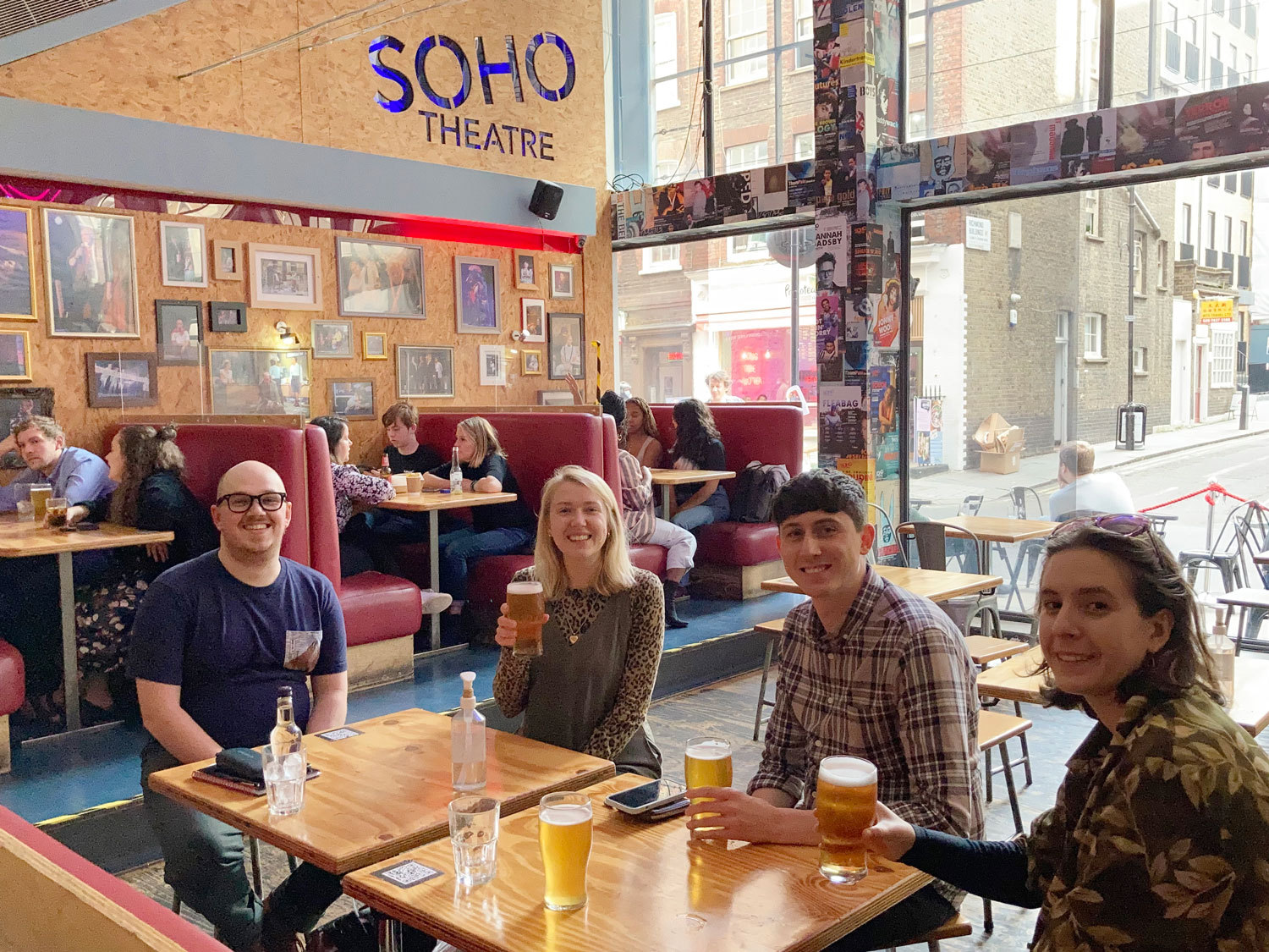 Four members of the Cog team sit at a table smiling and holding drinks at the Soho Theatre bar