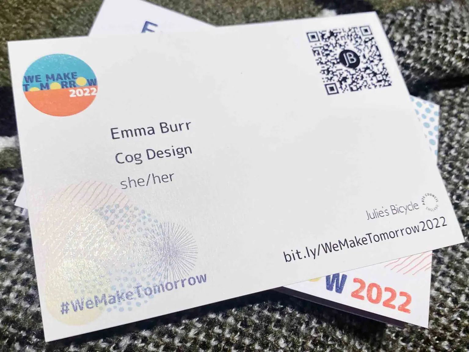 Two postcard sized pieces of thin card lie on top of each other. On the top card we can read Emma Burr, Cog Design, she/her