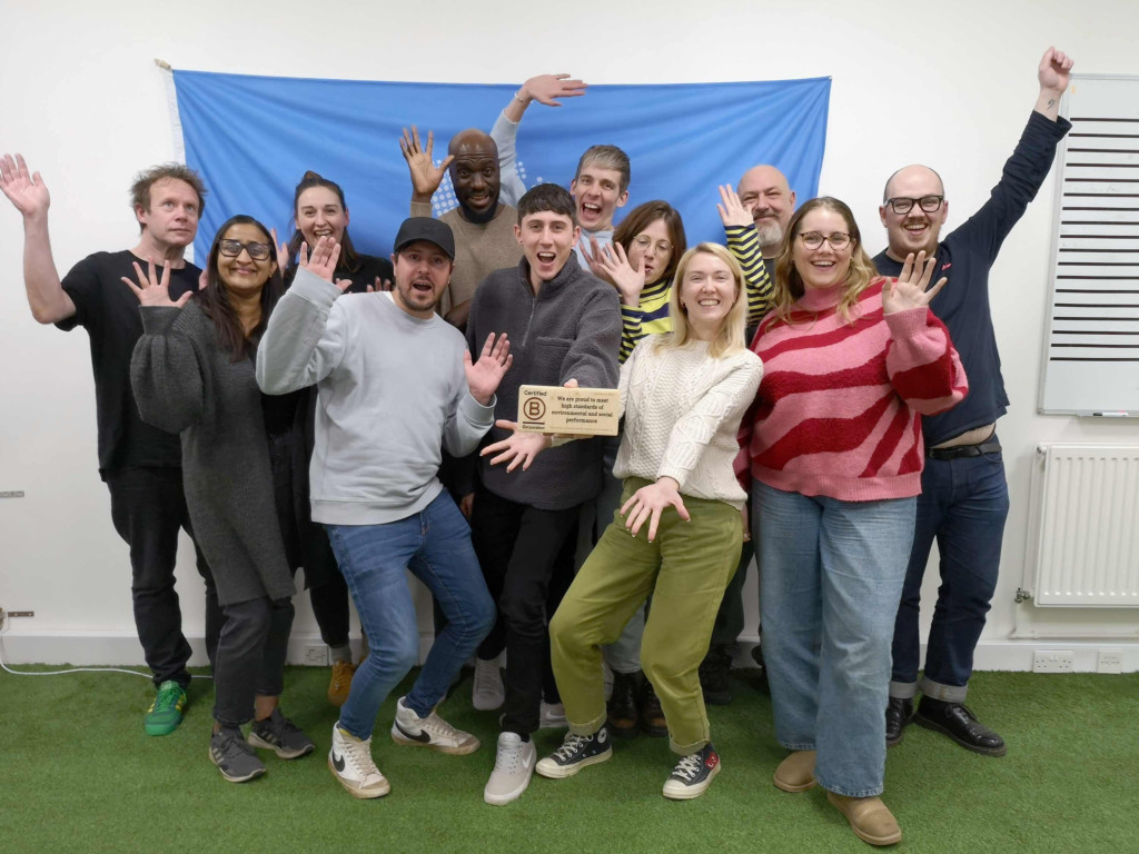 Group of people on fake grass smiling at the camera holding a wooden plaque