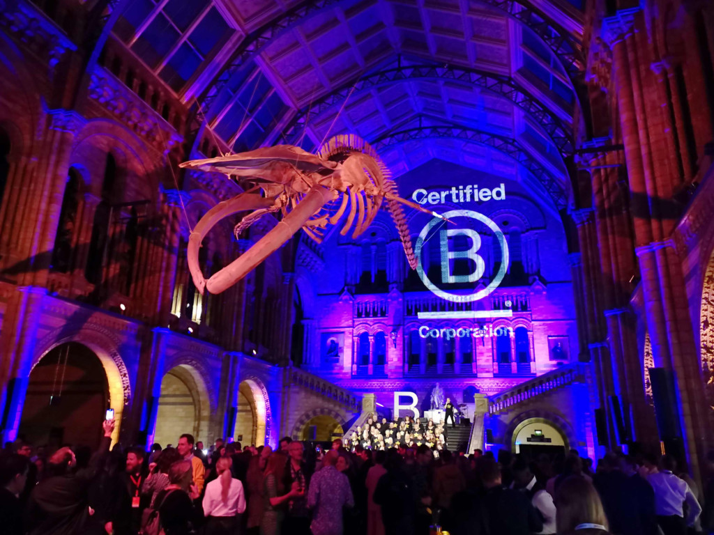 Large skeletal structure suspended from the ceiling in a purple-lit grand hall with lots of people below