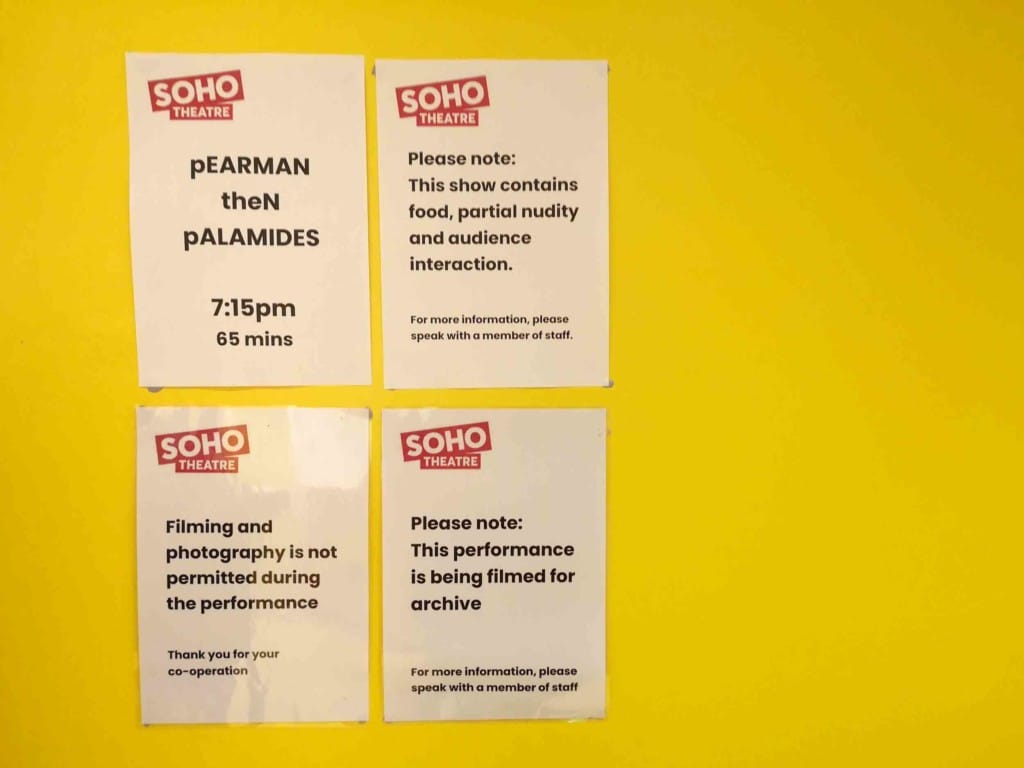 Four A4 sheets of paper are blue-tacked to a yellow wall. Each of them has a notice about the pearman then palamides show. They include disclaimers about the content and notification that the show is being filmed.