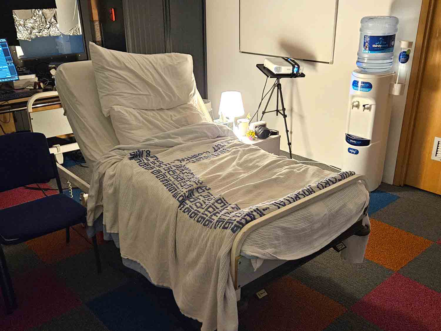 The hospital bed with Ayers's many admission dates embroidered into the blanket