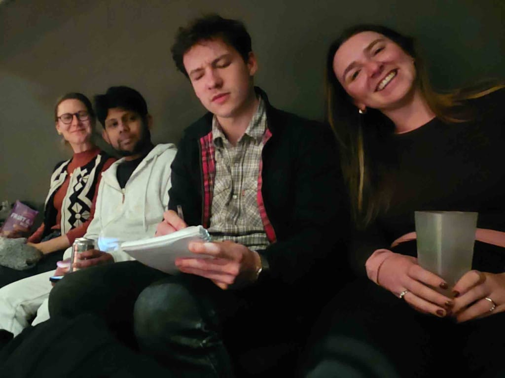 Four people in theatre seats, one of writing in a notebook.