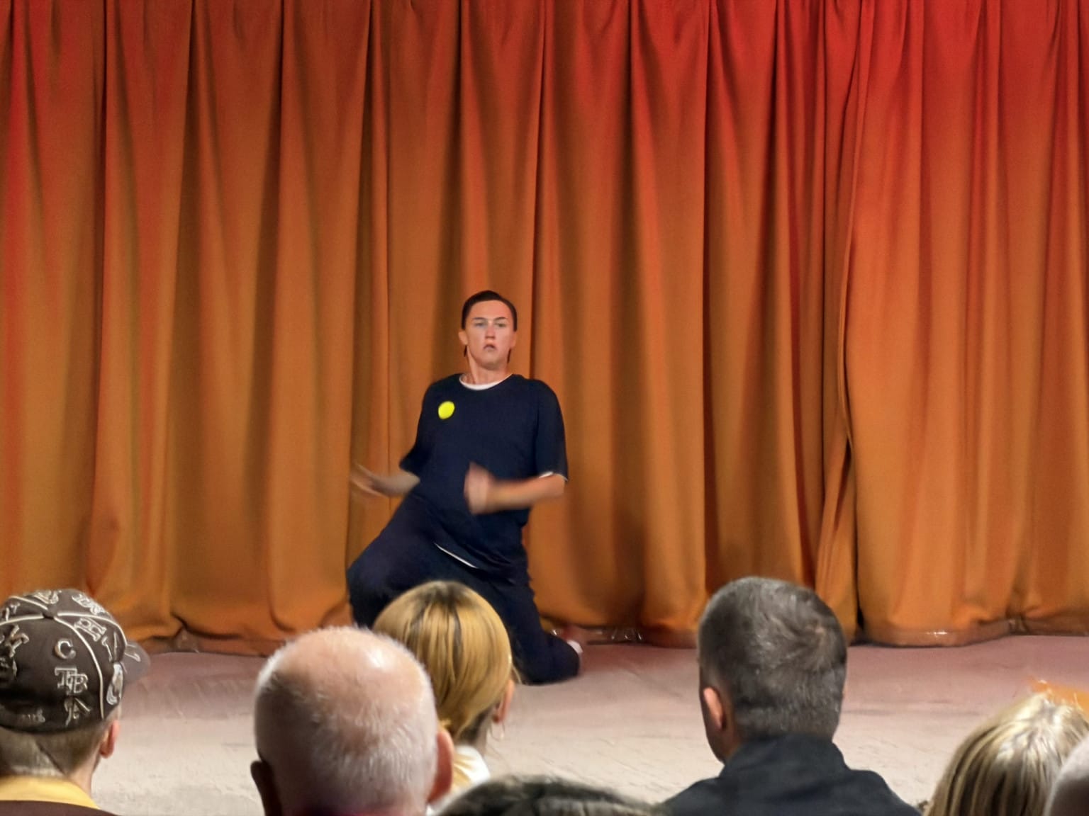 A blurred in motion picture of dancer in blue on their knees in front of an orange curtain