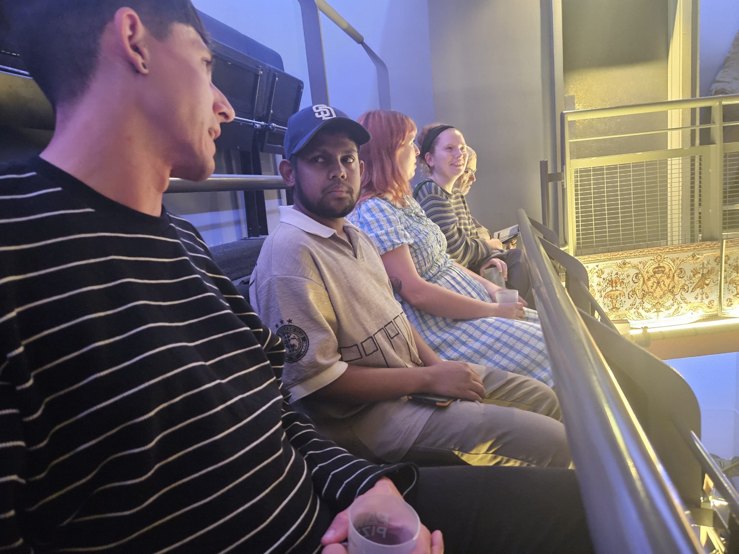 A row of people site behind a railing in a theatre's upper circle.